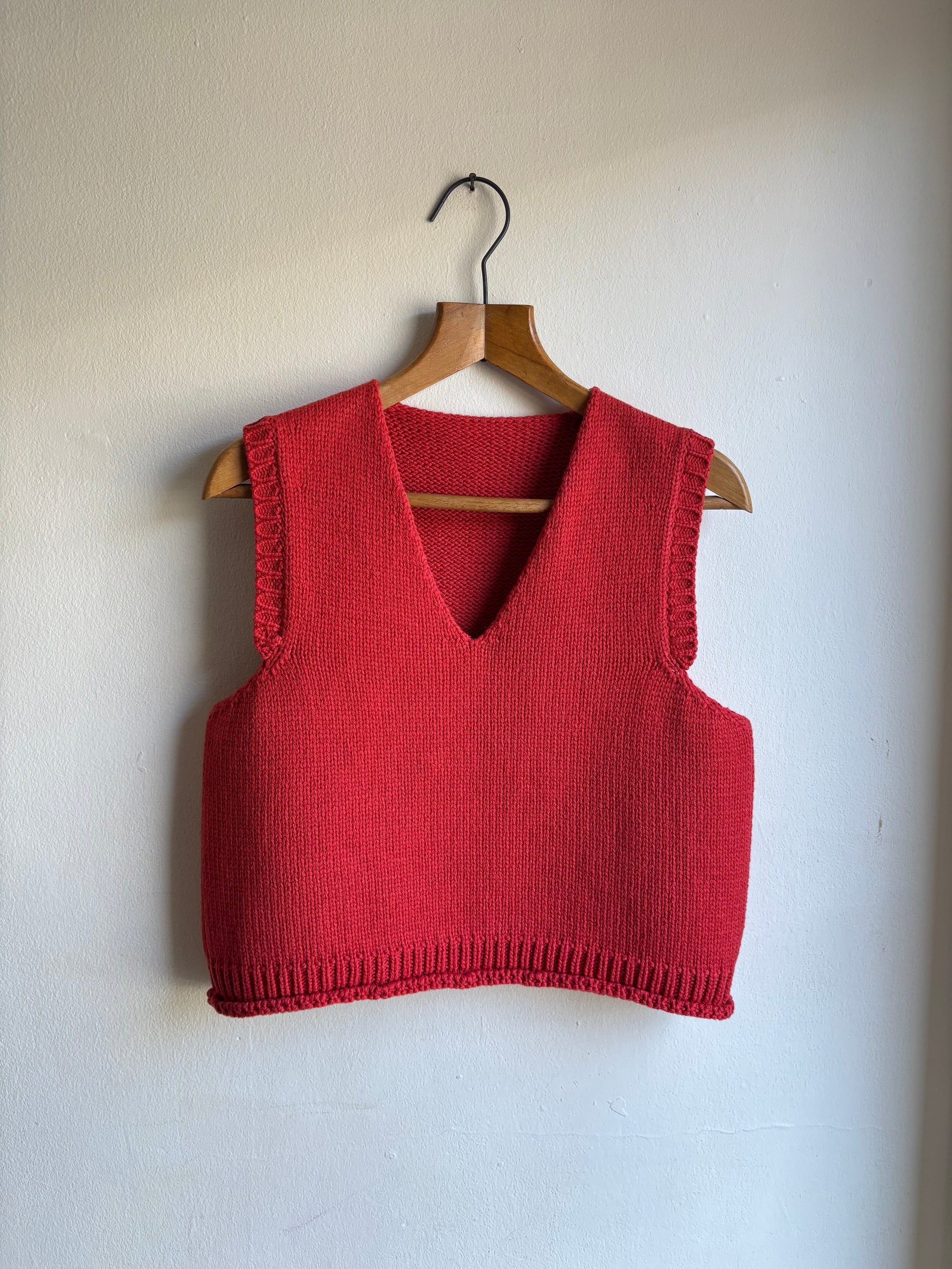 Red knitted vest on a wooden hanger against a white wall