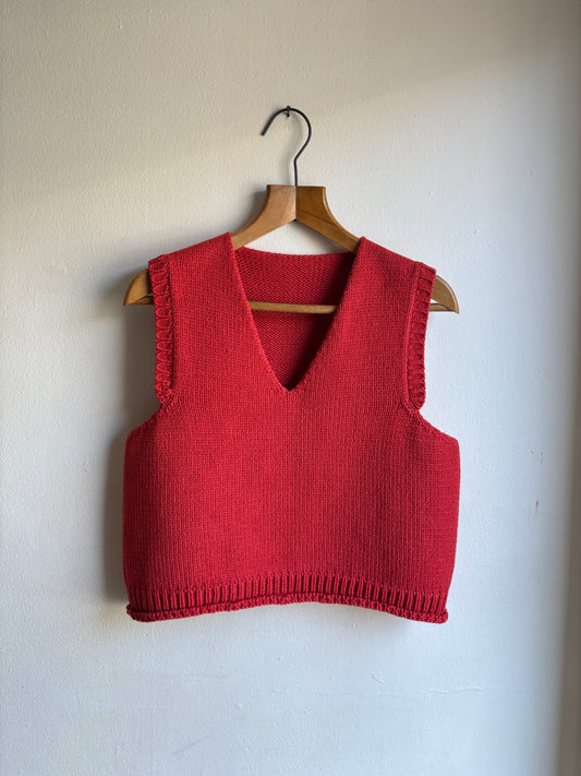 Red knitted vest on a wooden hanger against a white wall